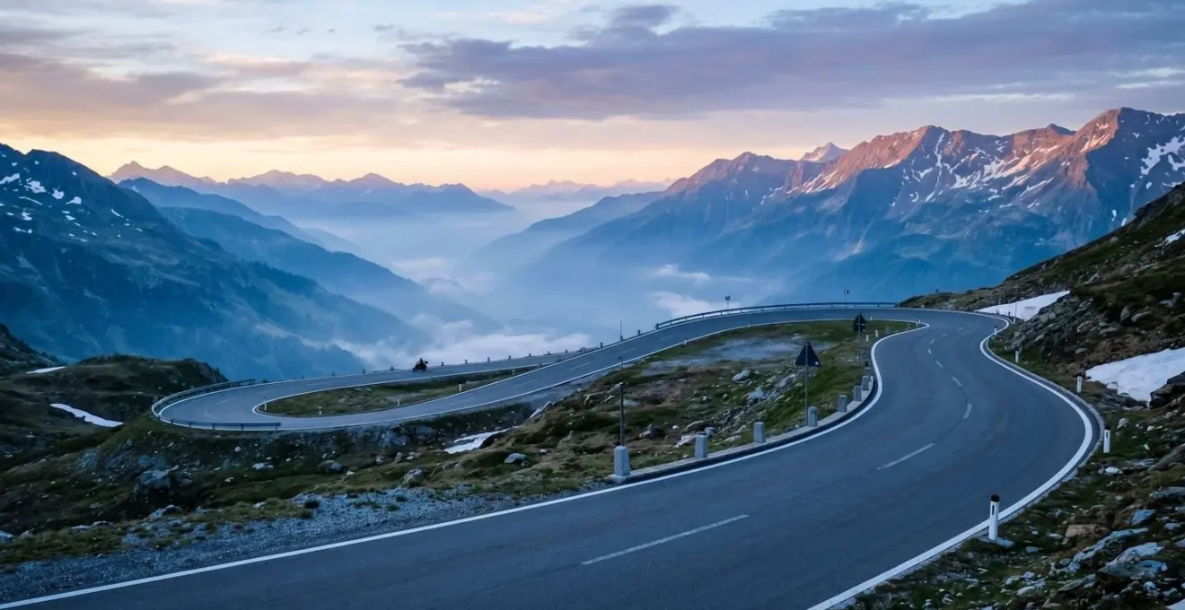 Einsame Passstrasse in den frühen Morgenstunden mit leichtem Nebel und erstem Sonnenlicht über den Berggipfeln