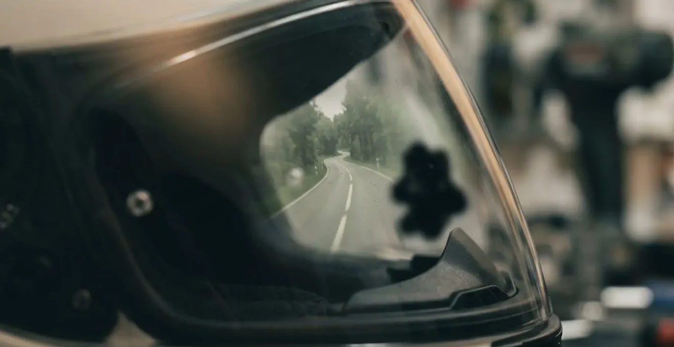 Nahaufnahme eines Motorradfahrer-Visiers mit Spiegelung einer Kurve und Strassenhindernis im peripheren Sichtfeld